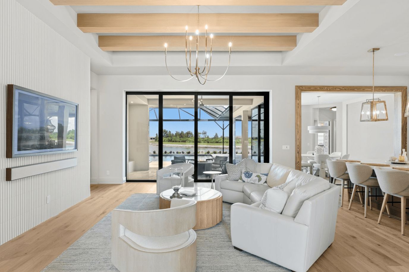 Natural light-wood beams across a white ceiling in an open living and dining room with chandeliers