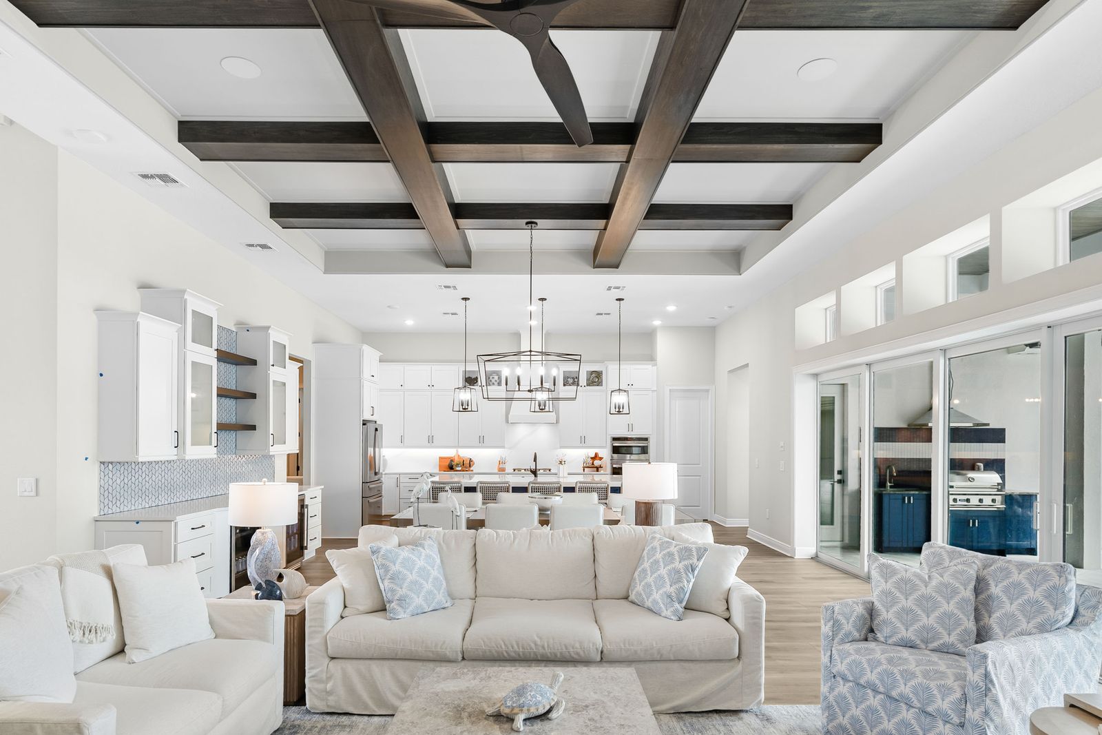 Great room with a grid of dark stained wood beams on a white ceiling above a light, coastal living area