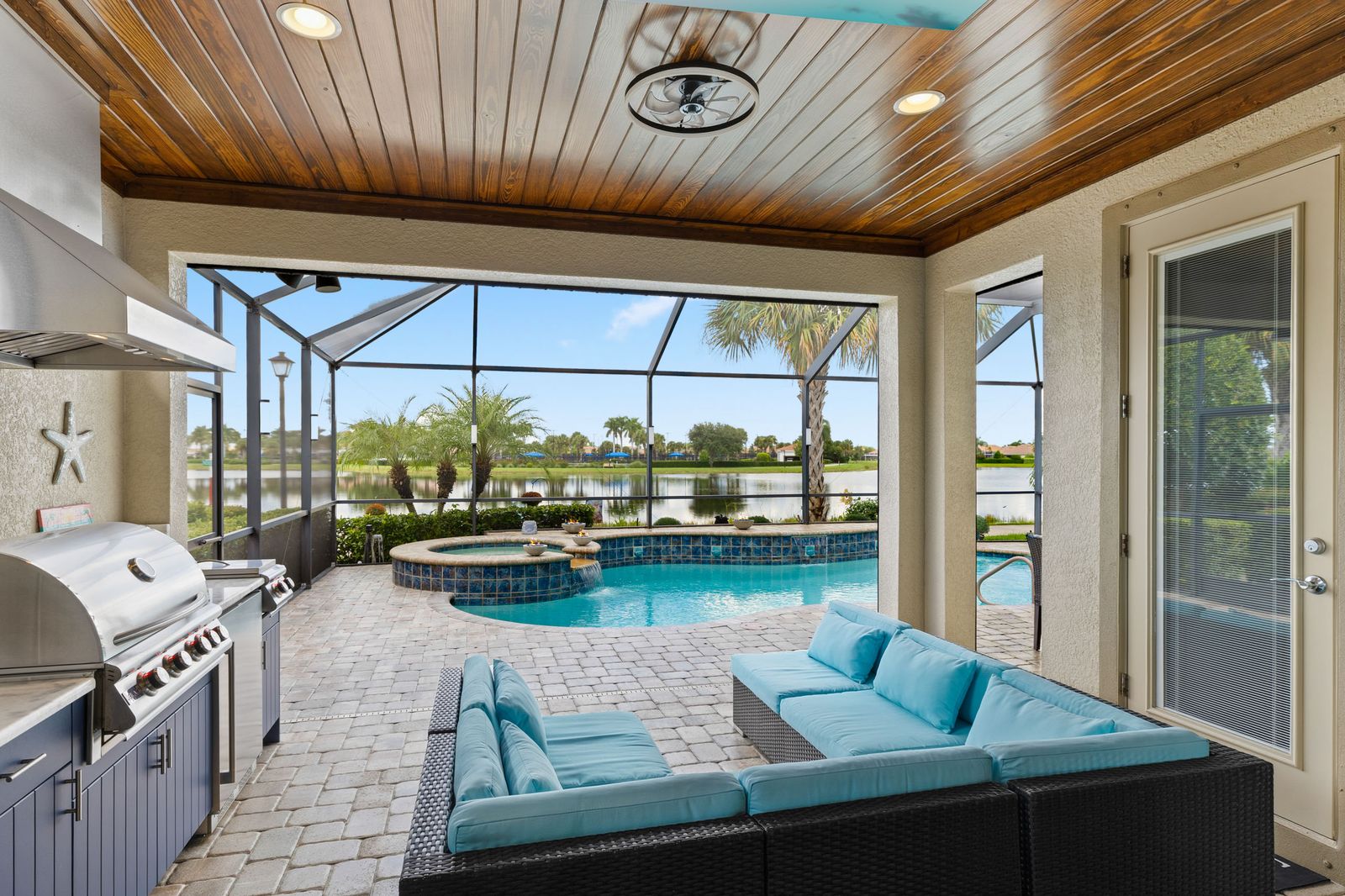 Covered lanai with a stained tongue-and-groove wood ceiling over an outdoor kitchen and dining table, open to a screened pool